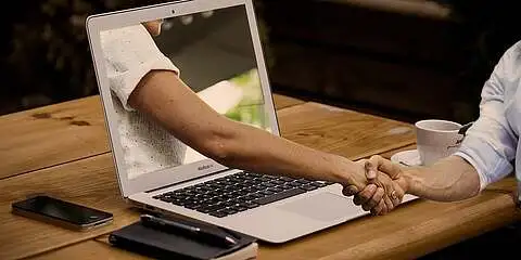Hybrides Training: Handschlag zwischen zwei Personen über den Laptop