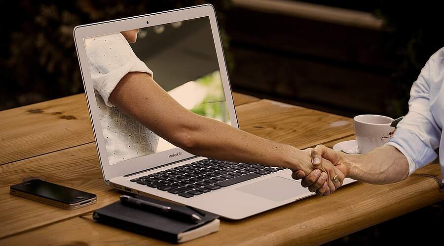 Hybrides Training: Handschlag zwischen zwei Personen über den Laptop Hybrides Training: Handschlag zwischen zwei Personen über den Laptop