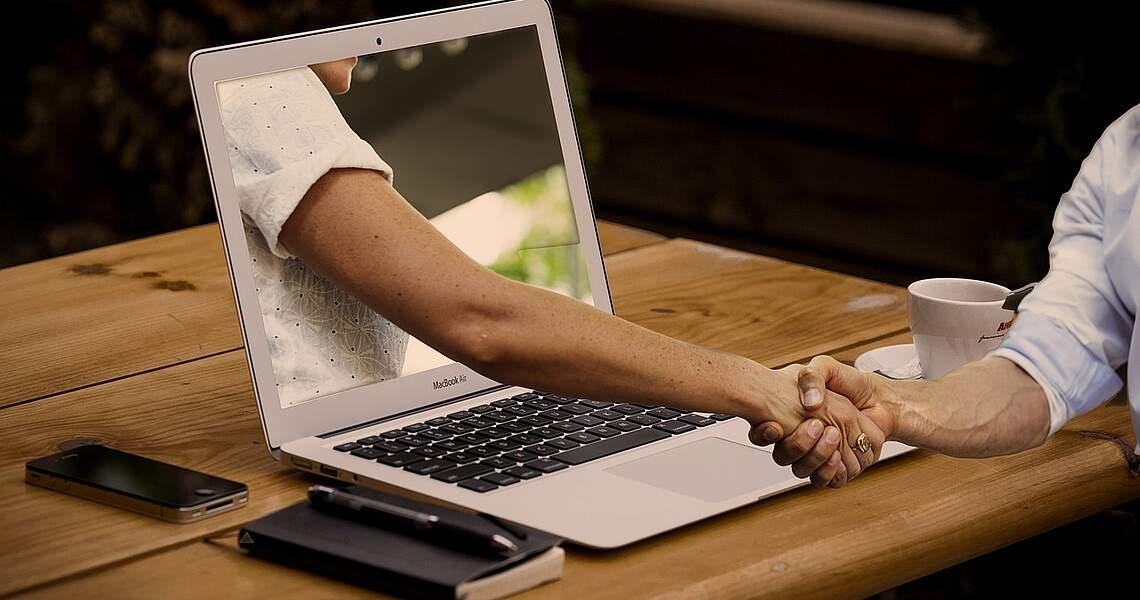 Hybrides Training: Handschlag zwischen zwei Personen über den Laptop Hybrides Training: Handschlag zwischen zwei Personen über den Laptop